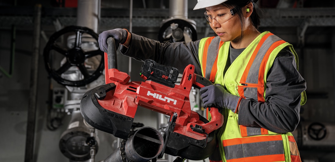 Mujer usando una sierra de cinta para cortar un tubo de metal